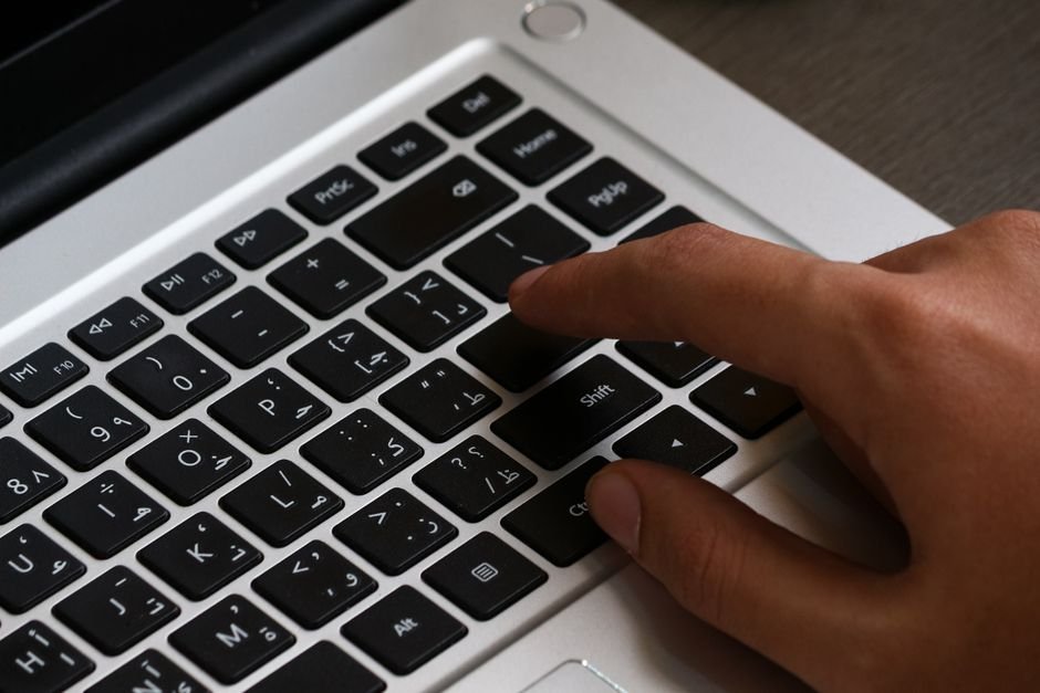 Hands typing on a multilingual keyboard, illustrating the transliteration problem in Bangla content moderation